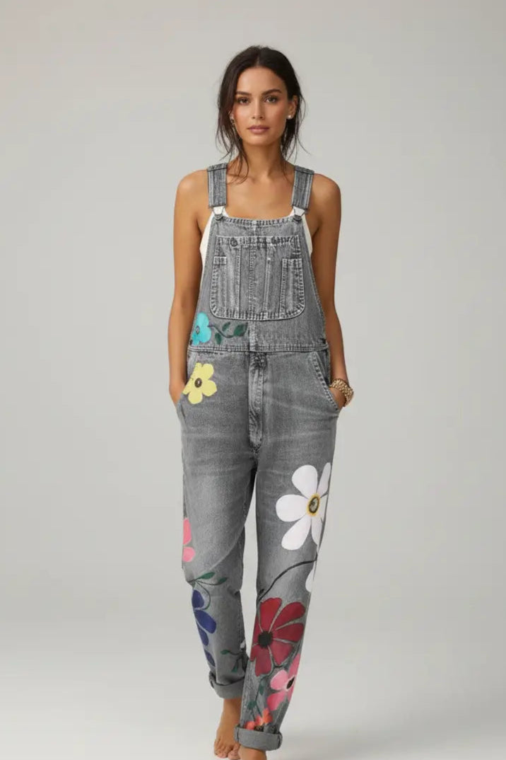 Woman wearing gray denim overalls with colorful floral designs on a plain background
